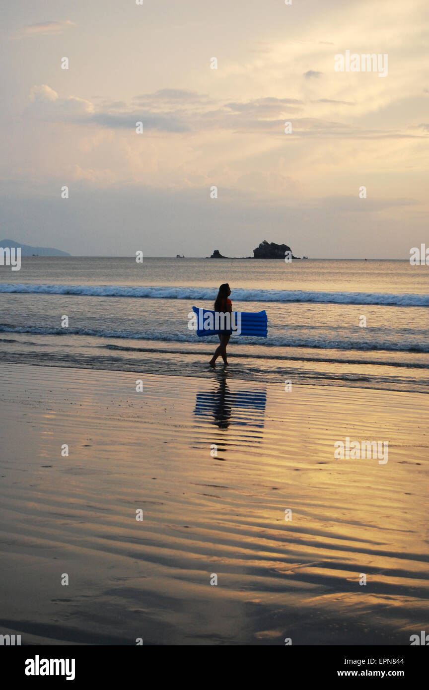 Una persona a piedi in mare al tramonto tenendo un lilo sulla spiaggia di Koh Phayam Thailandia Foto Stock