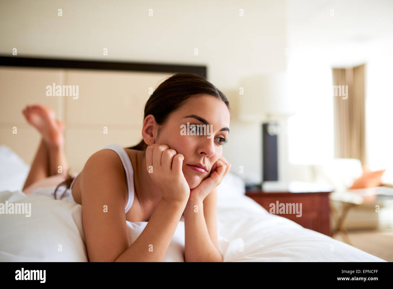 Attraente donna giaceva a letto in appoggio mento in mani cercando triste. Foto Stock