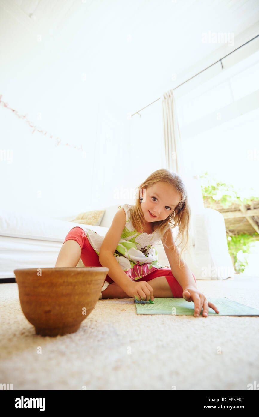 Ritratto di ragazza in età prescolare colorazione immagine sul pavimento nella sua casa. Giovane ragazza seduta sul pavimento la pittura di un'immagine. Foto Stock