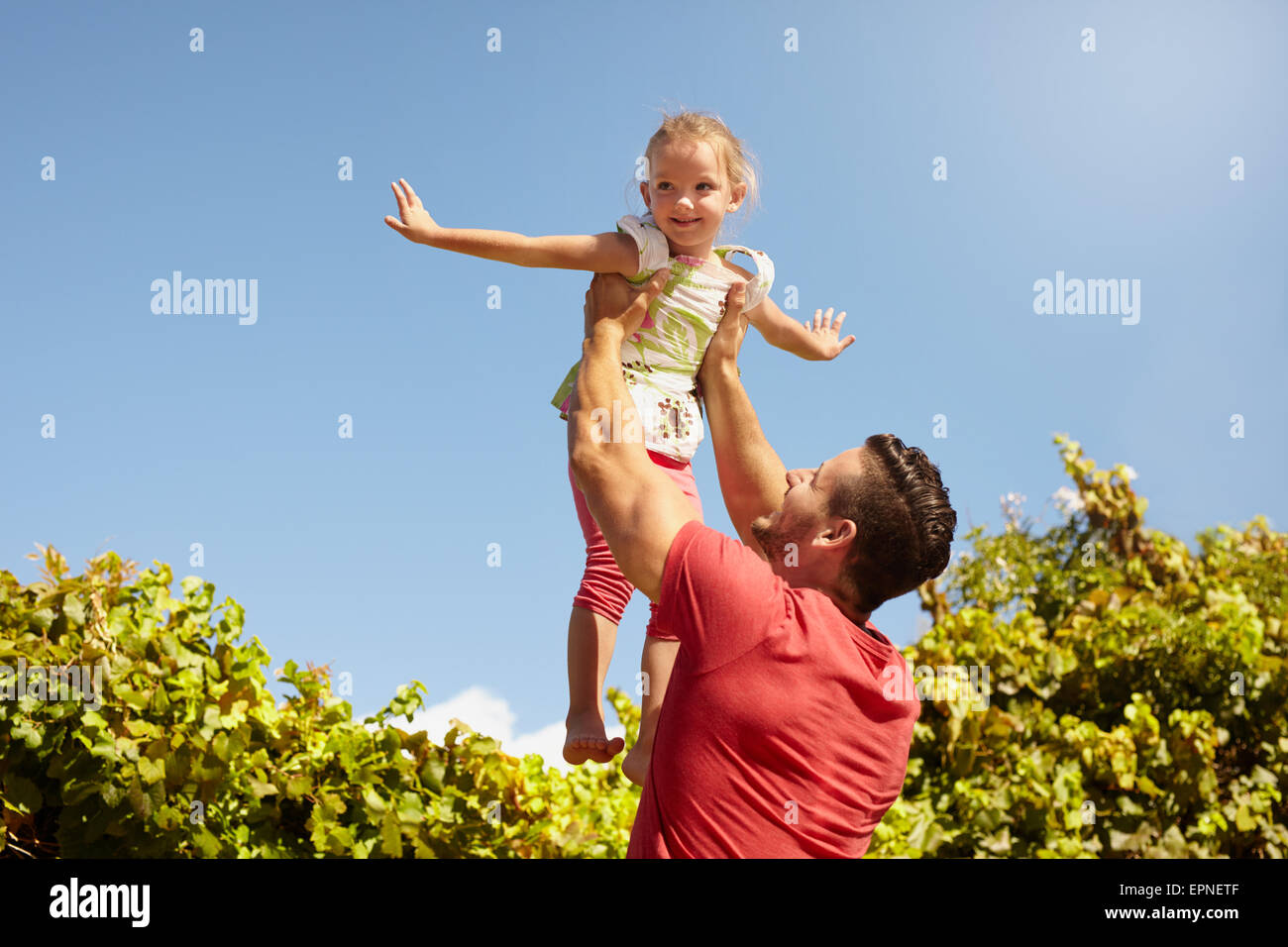 Bambina fingendo di essere un velivolo come suo padre il suo ascensore nell'aria. Padre tenendo la sua figlia fino ad alta contro il cielo. Foto Stock