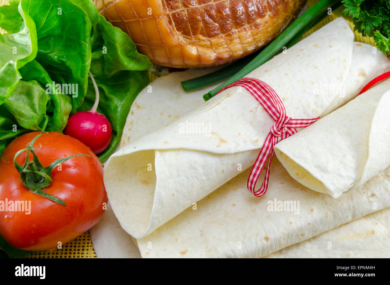 Svuotare tortillas legate con un nastro rosso su un tavolo con il pomodoro, la lattuga e prosciutto Foto Stock