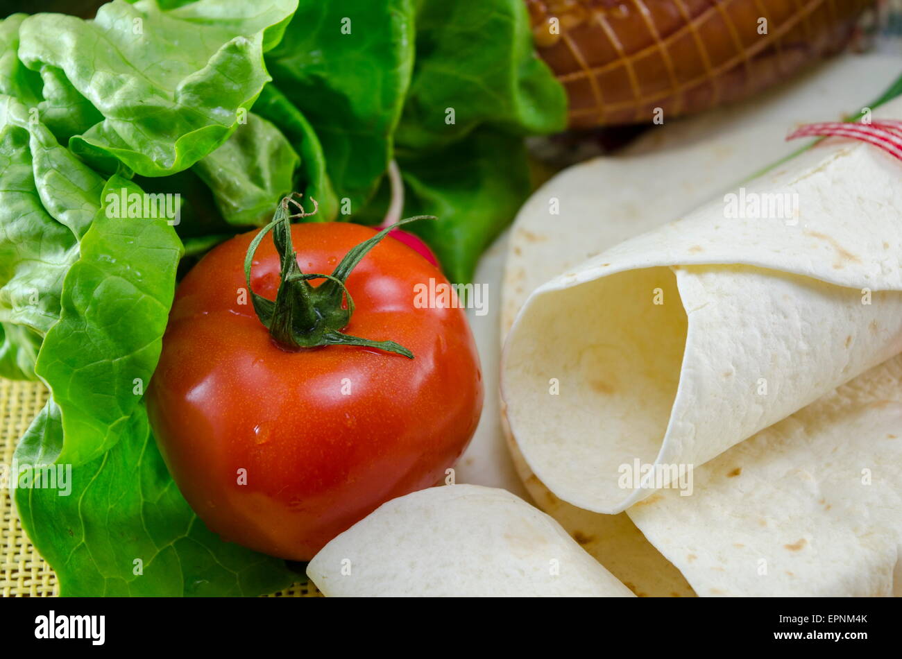 Svuotare tortillas legate con un nastro rosso su un tavolo con il pomodoro, la lattuga e prosciutto Foto Stock