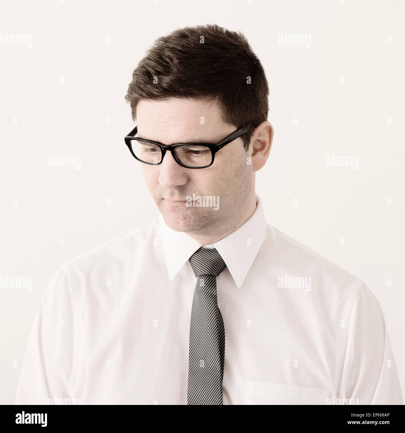 Ritratto di imprenditore con occhiali, una camicia bianca e cravatta in ufficio. Egli è guardando in giù con un espressione seria. Foto Stock