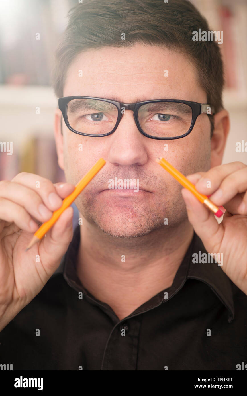 Ritratto di uomo serio con gli occhiali tenendo una matita rotto nella parte anteriore del suo volto. Foto Stock