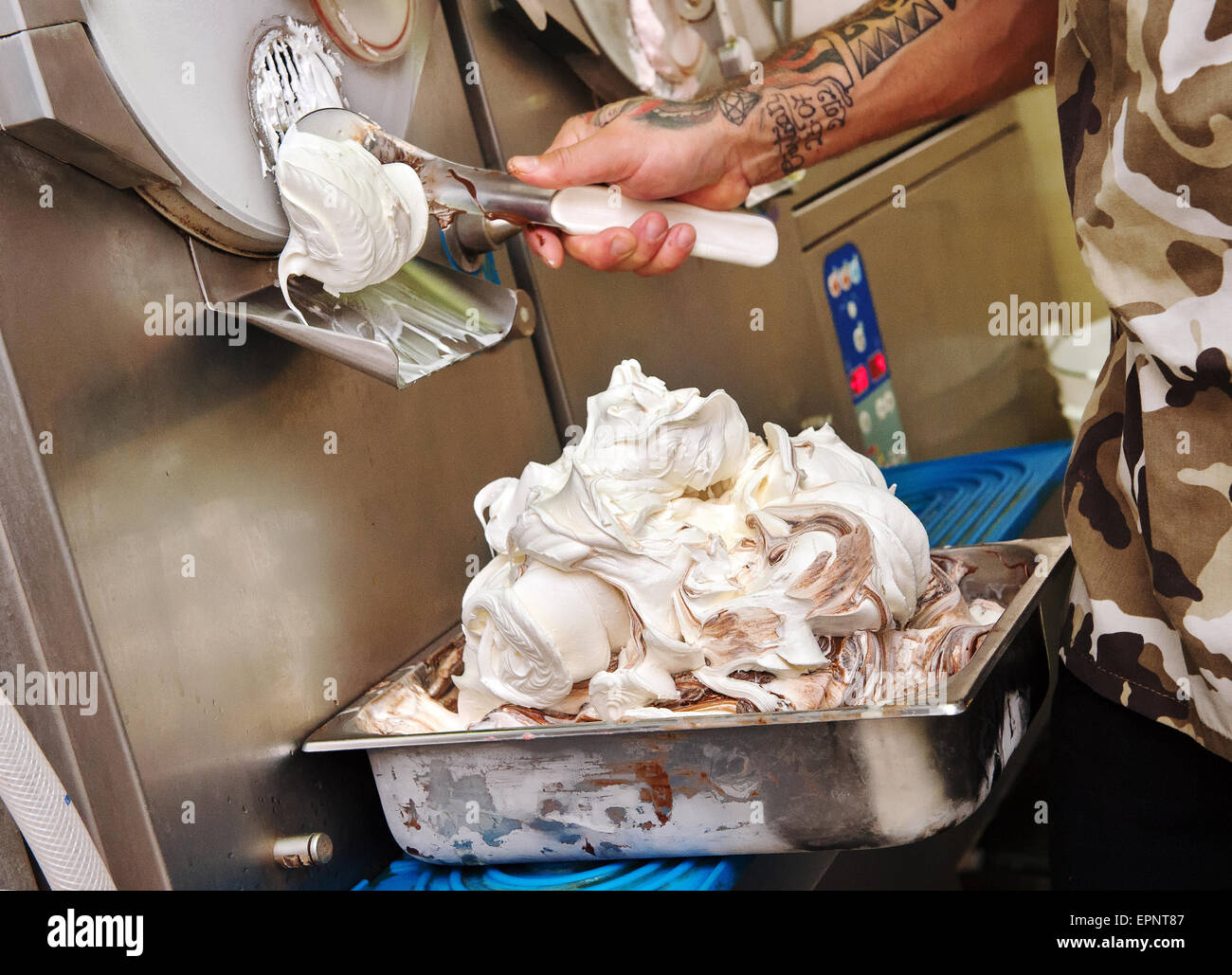 L'uomo facendo artigianale di gelato usando un acciaio inossidabile zangola industriale erogazione del dessert freschi su un vassoio per la vendita come prendere Foto Stock