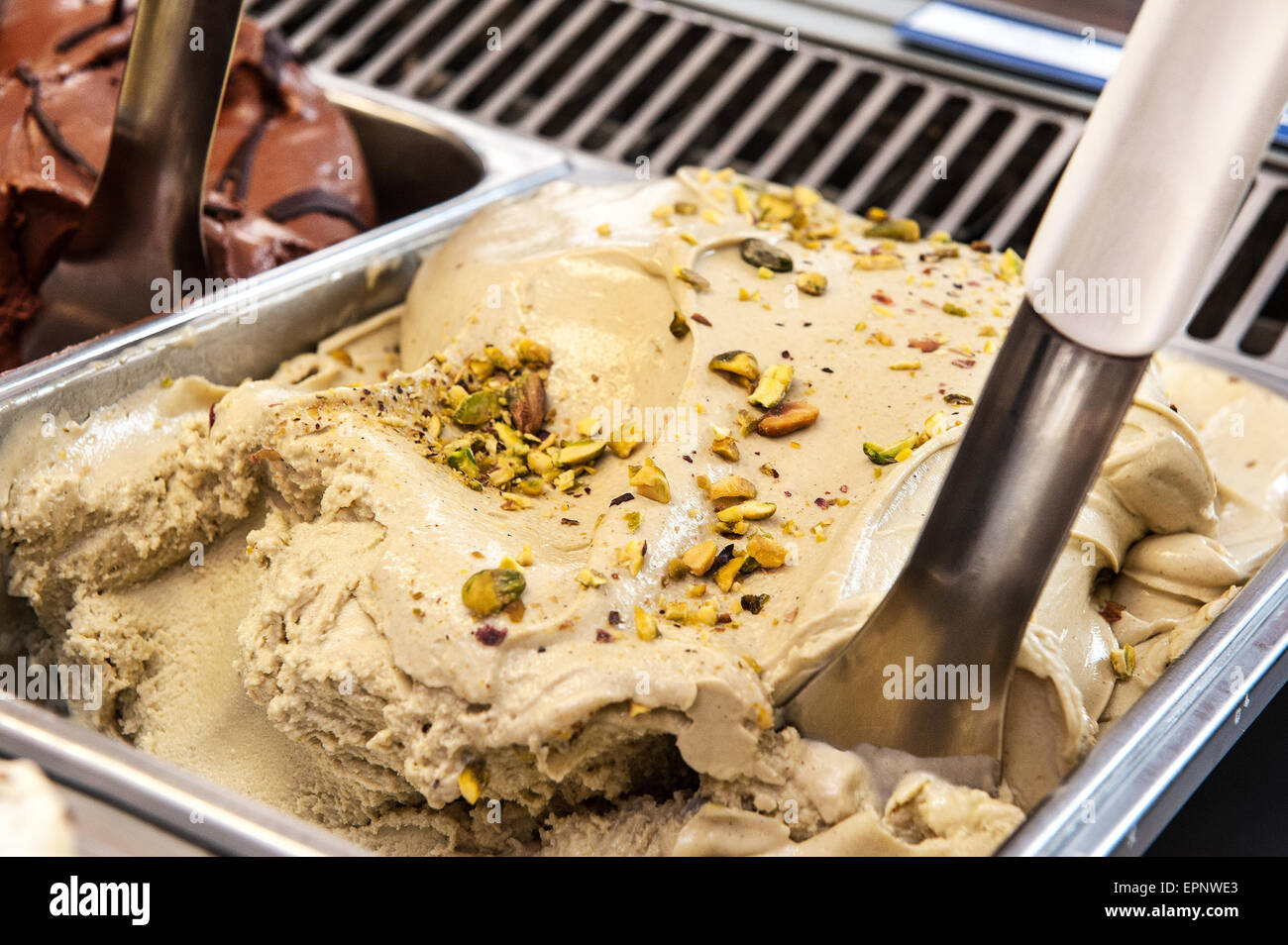 Deliziosa di noce pistacchio gelato cosparso con noci tostate sul display in una gelateria con un cucchiaio per la vendita come prendere Foto Stock