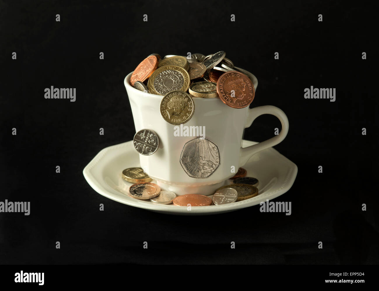 'My cup corre su un bicchiere di bianco e il piattino pieno di GBP British monete fuoriuscita.Un REGNO UNITO denaro economia finanza monete ricchezza Foto Stock
