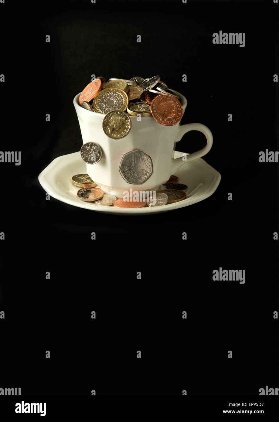 'My cup corre su un bicchiere di bianco e il piattino pieno di GBP British monete fuoriuscita.Un REGNO UNITO denaro economia finanza monete ricchezza Foto Stock