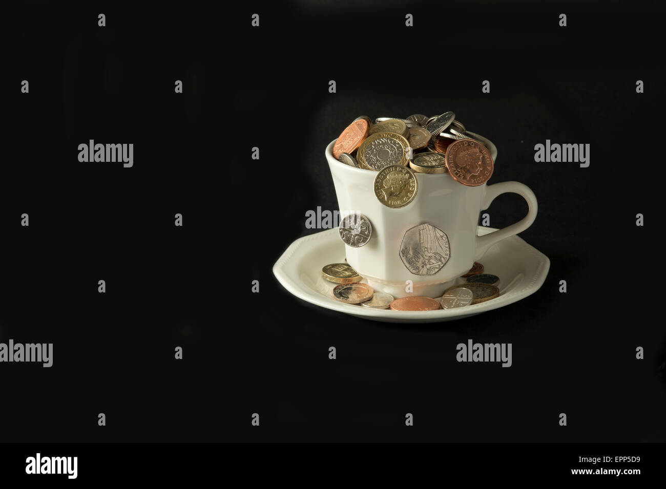 'My cup corre su un bicchiere di bianco e il piattino pieno di GBP British monete fuoriuscita.Un REGNO UNITO denaro economia finanza monete ricchezza Foto Stock