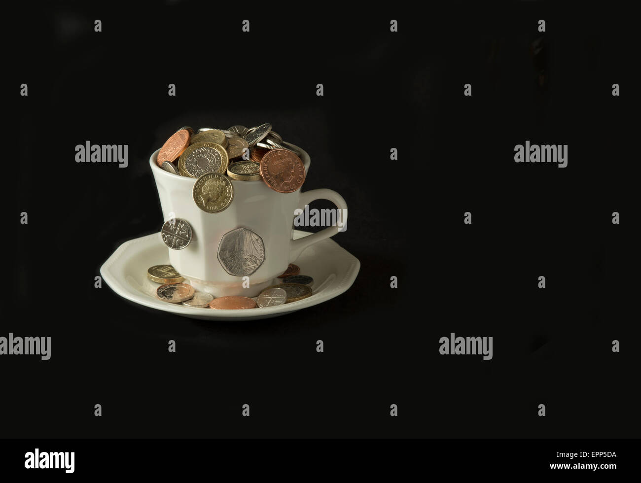 'My cup corre su un bicchiere di bianco e il piattino pieno di GBP British monete fuoriuscita.Un REGNO UNITO denaro economia finanza monete ricchezza Foto Stock