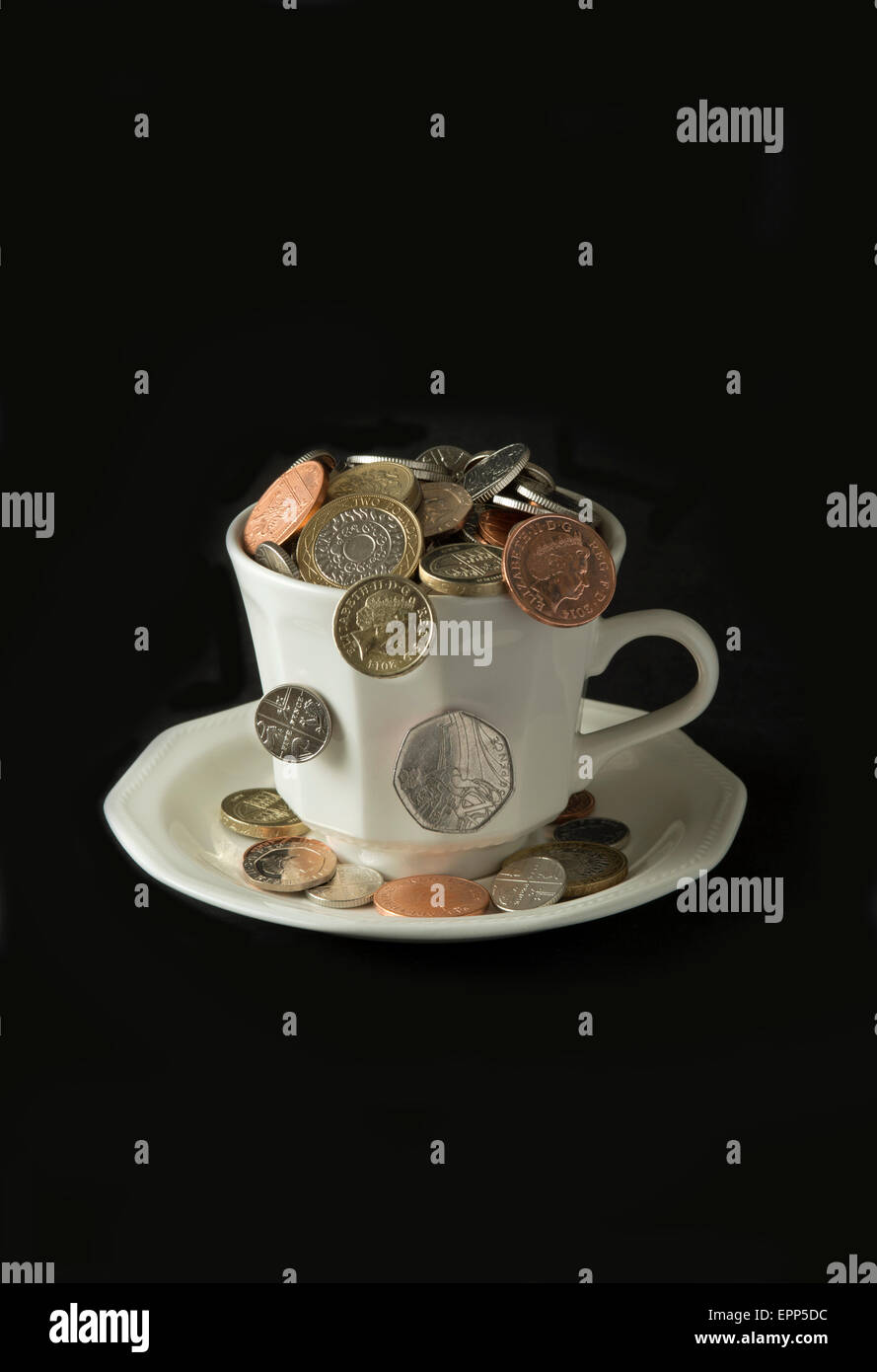 'My cup corre su un bicchiere di bianco e il piattino pieno di GBP British monete fuoriuscita.Un REGNO UNITO denaro economia finanza monete ricchezza Foto Stock