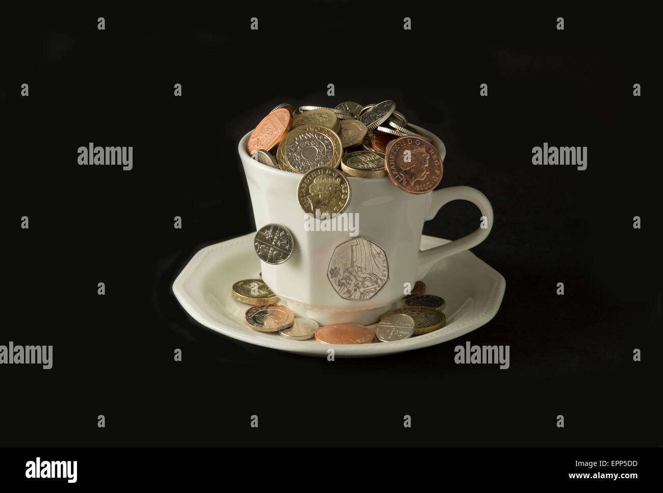 'My cup corre su un bicchiere di bianco e il piattino pieno di GBP British monete fuoriuscita.Un REGNO UNITO denaro economia finanza monete ricchezza Foto Stock