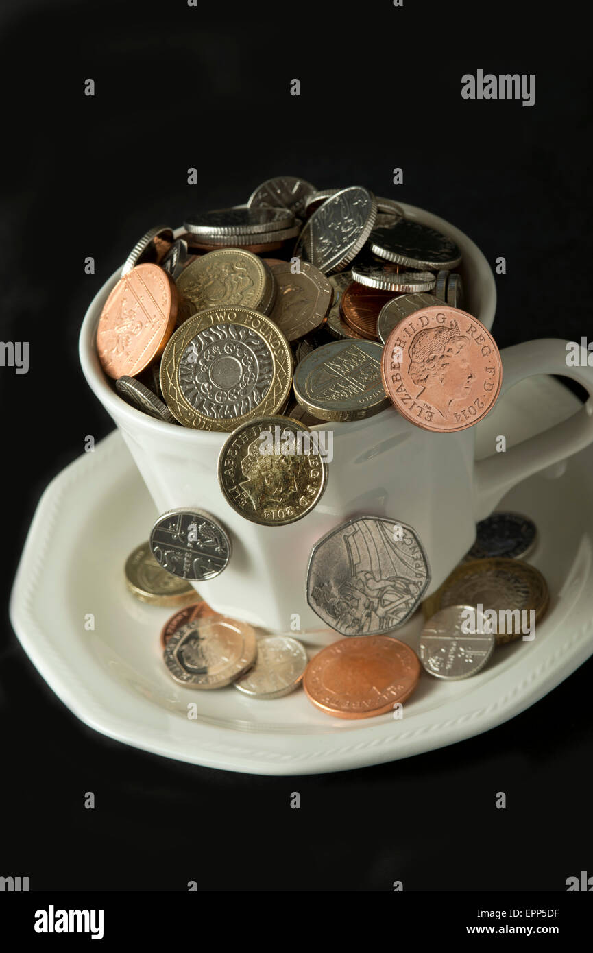 'My cup corre su un bicchiere di bianco e il piattino pieno di GBP British monete fuoriuscita.Un REGNO UNITO denaro economia finanza monete ricchezza Foto Stock