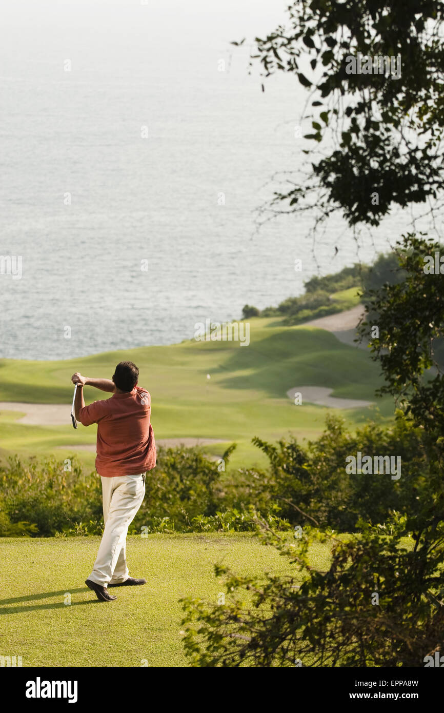 Un uomo gioca a golf a El Tamarindo con l'oceano sullo sfondo. Foto Stock