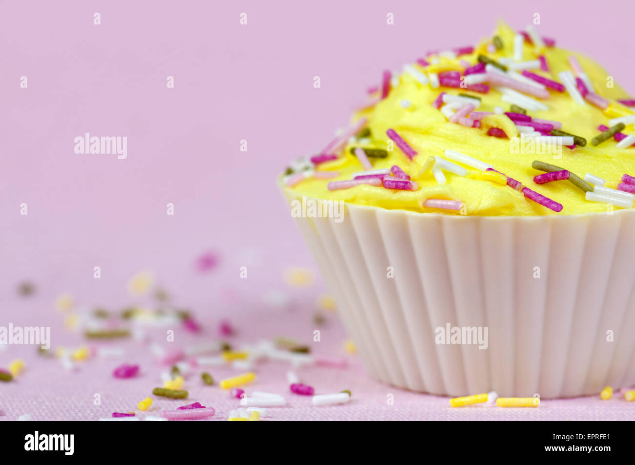 Piuttosto decorato in maniera colorata cupcake o fata la torta con la glassa di colore giallo e spruzzi di colore su un sfondo rosa Foto Stock