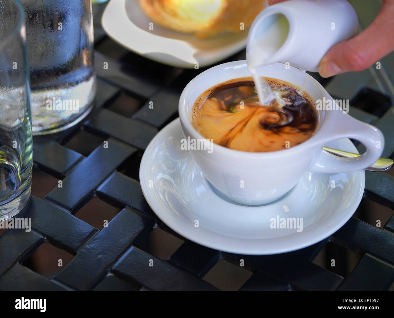 La crema che viene versato in caffè in tazza bianca con piattino in outdoor, patio tavolo, Canada Foto Stock