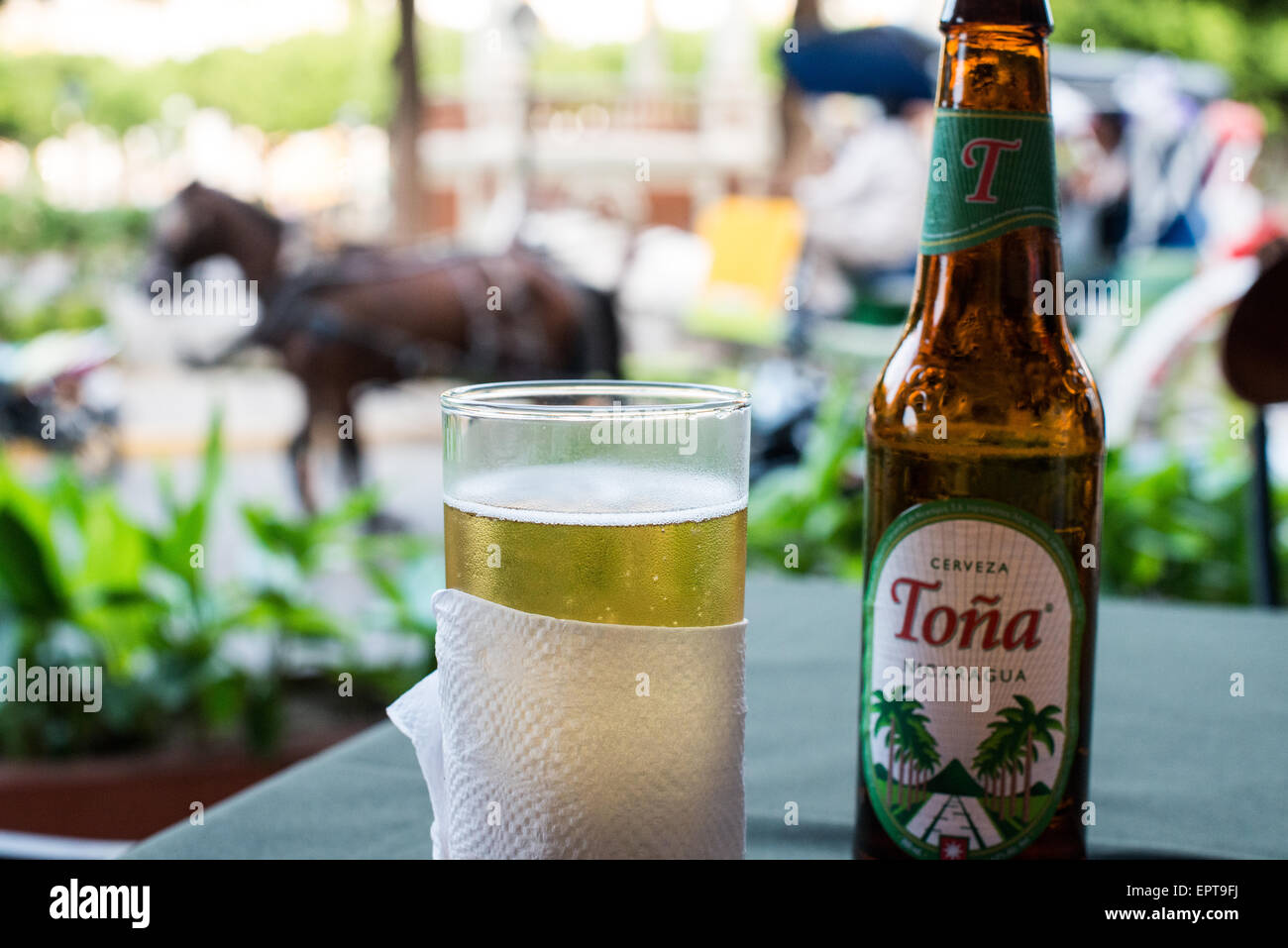 GRANADA, Nicaragua - Un bicchiere di Toña Cerveza a un tavolo che si affaccia sul Parque Central, con una carrozza trainata da cavalli che passa sullo sfondo. Parque Central è la piazza principale e il cuore storico di Granada, Nicaragua. Foto Stock