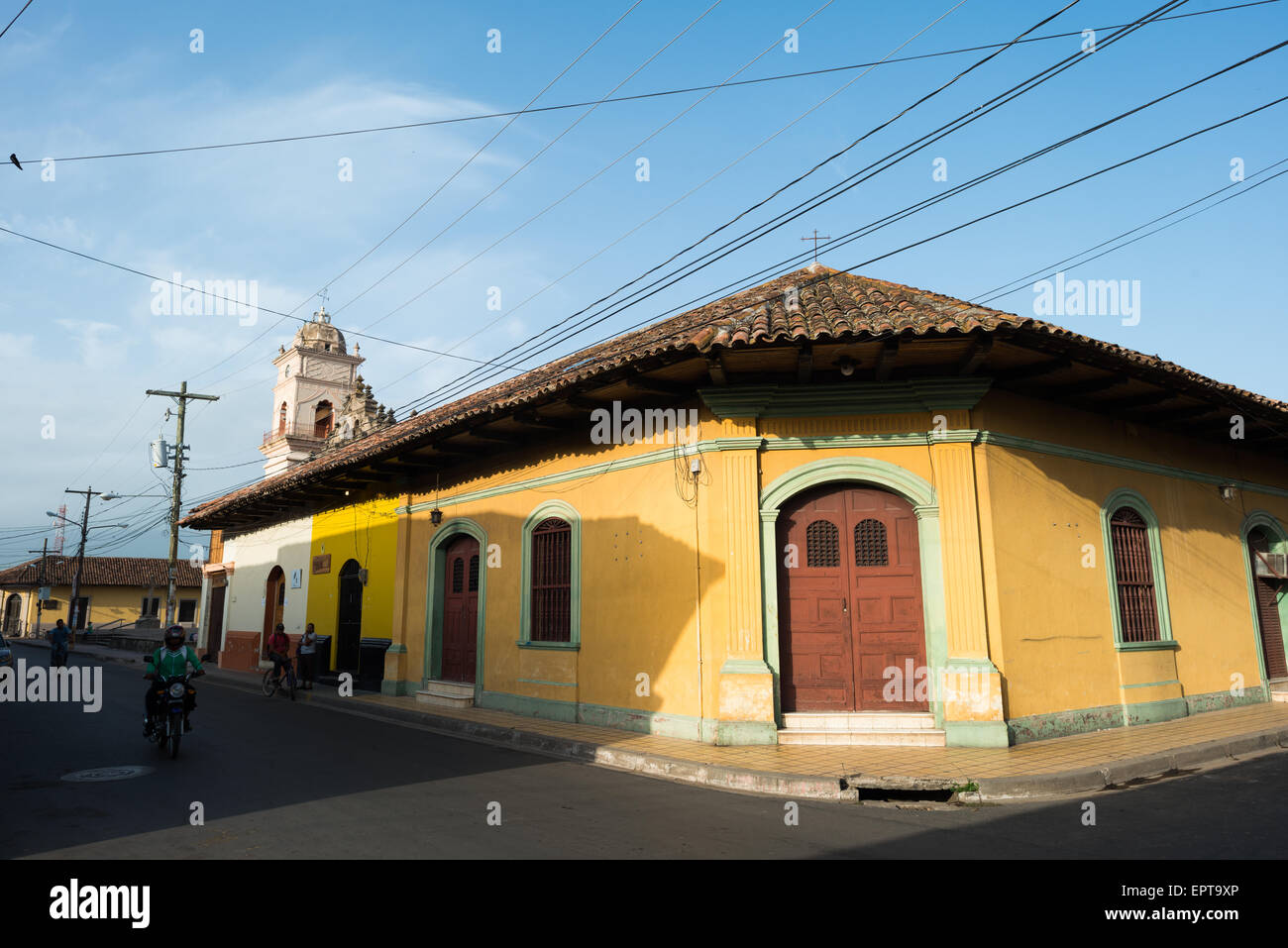 Edificio d'angolo coloniale spagnolo giallo con tetto in tegole di terracotta Granada Nicaragua | GRANADA, Nicaragua — Un edificio giallo con tetto in tegole di terracotta incontra il suo vicino a un angolo di strada smussato, un segno distintivo dell'urbanistica coloniale spagnola. Il taglio angolare ha allargato l'incrocio in modo che i carri trainati da cavalli e le carrozze potessero svoltare senza graffiare la muratura, un design mantenuto nella griglia di Granada dalla sua fondazione nel 1524 da parte di Francisco Hernández de Córdoba. Foto Stock