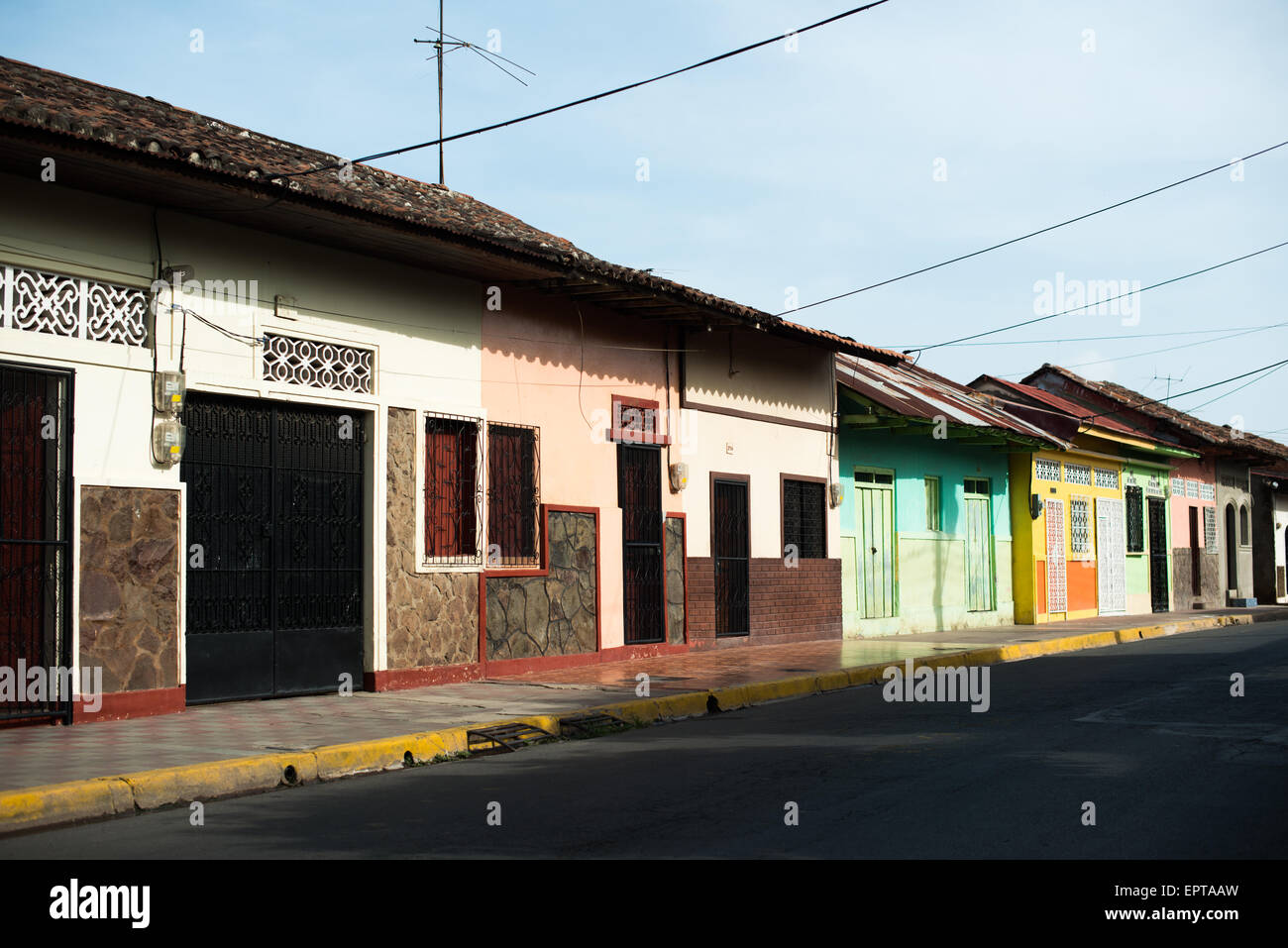 Case a schiera coloniali spagnole Facciate colorate Tetti di tegole Granada Nicaragua | GRANADA, Nicaragua — Case a schiera coloniali dipinte di colori vivaci con tetti di terracotta sporgenti costeggiano una strada nel centro storico, le loro facciate continue seguono la griglia originale tracciata quando la città fu fondata nel 1524. Griglie di finestra in ferro battuto e prese d’aria aperte in muratura consentono una ventilazione sicura nel clima tropicale del bacino del Lago Nicaragua. Foto Stock