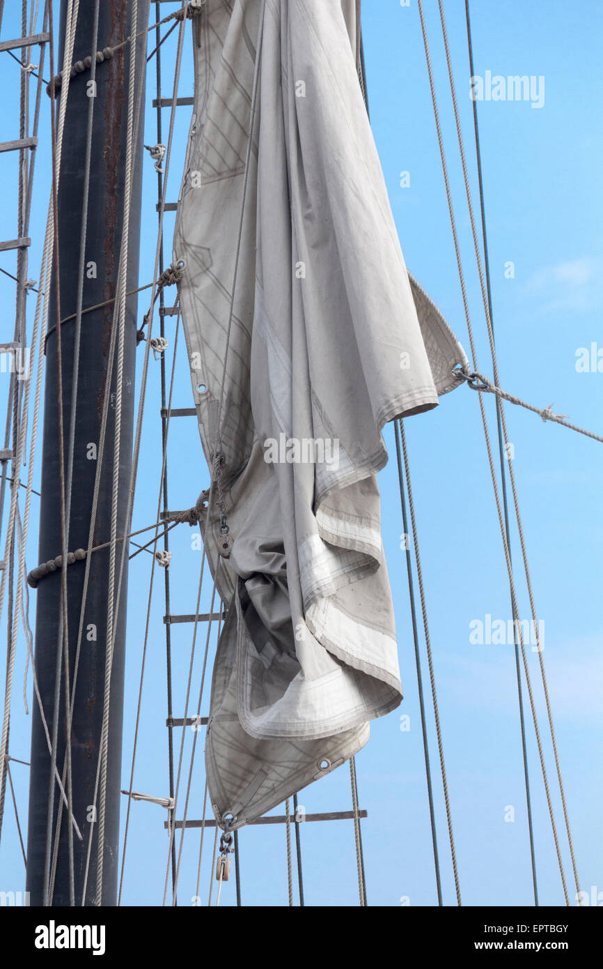 Legata giù la vela sul montante di un tall ship su una luminosa giornata soleggiata con cielo blu. Foto Stock
