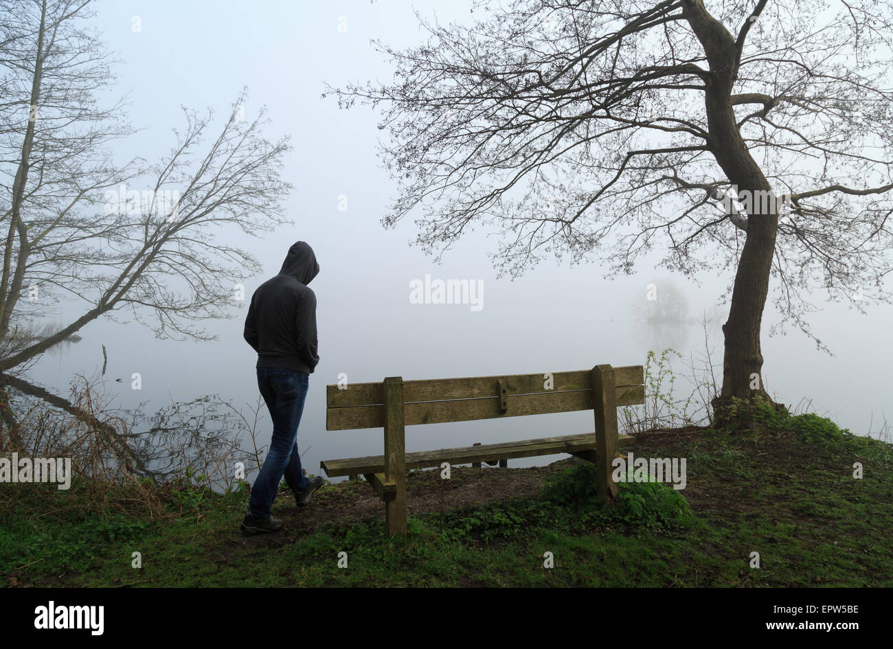La malinconia emozioni concetto: l'uomo che si avvicinano ad un banco a un lago in un giorno di nebbia. Foto Stock