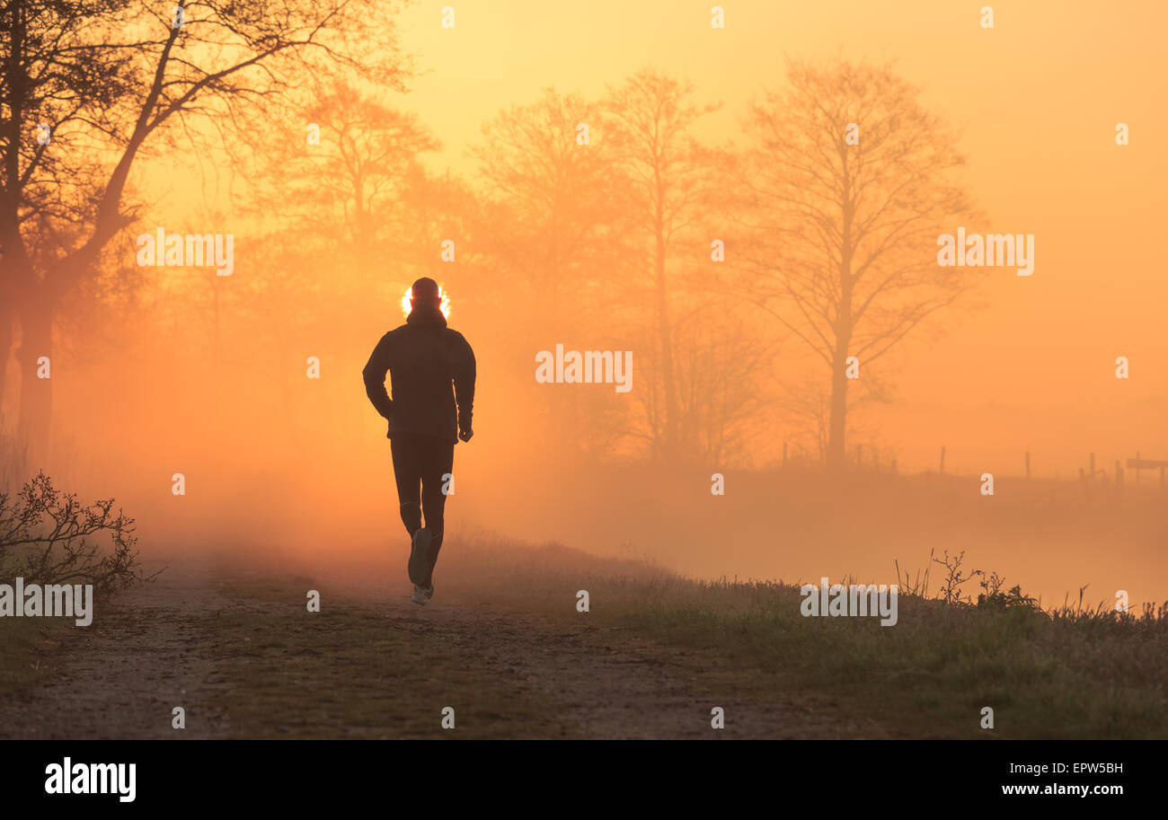 Il concetto di sport: runner su una strada di ghiaia durante una nebbia, molla sunrise in campagna. Foto Stock