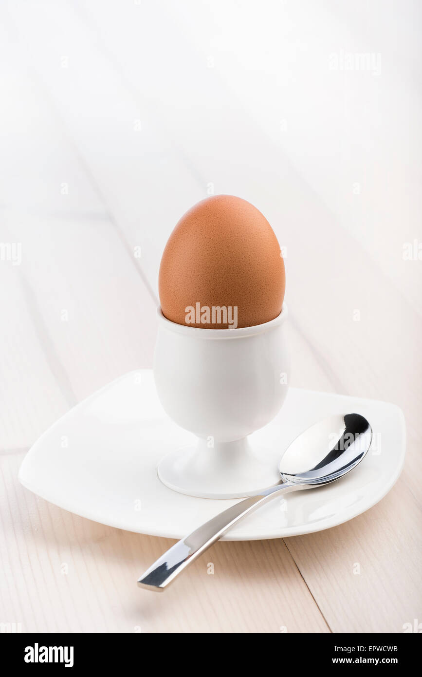 Eggcup con cucchiaino e uova sode, sul tavolo di legno Foto Stock