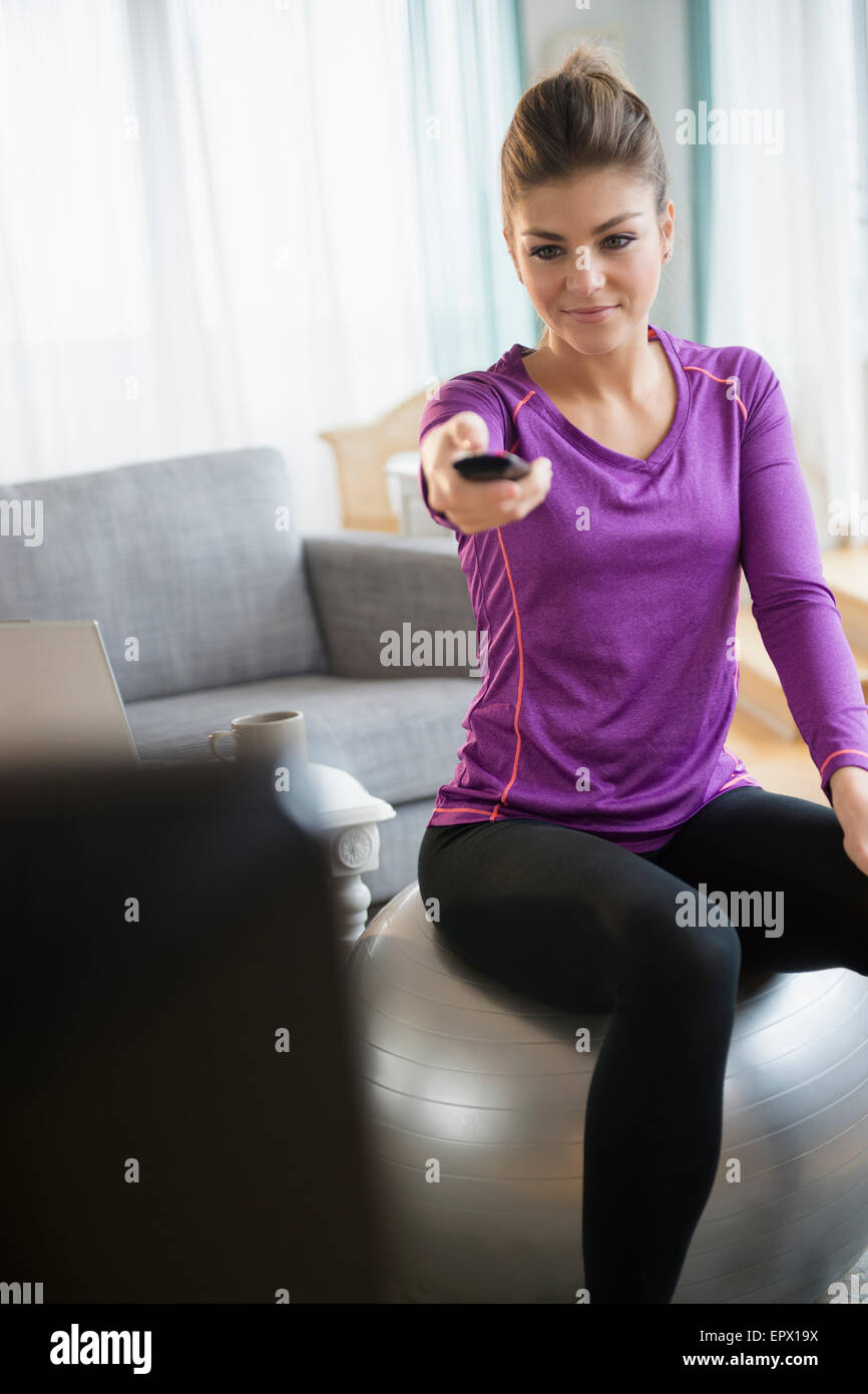 Giovane donna seduta su esercizio di palla e girando sulla tv Foto Stock