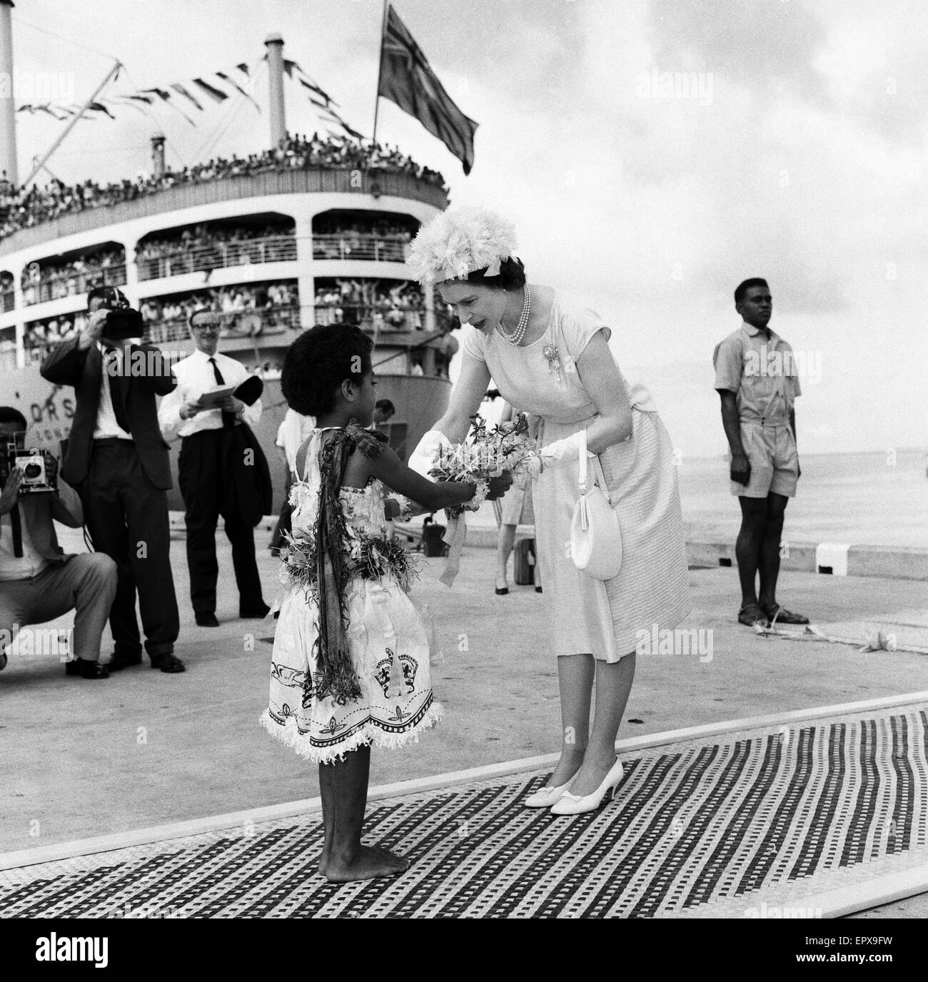 La regina Elisabetta II arriva a Suva Figi dal Royal Yacht e viene presentato un mazzo di fiori da ragazza Fijiano Kaunilotuma Adi che seduto di fronte a lei sul tappeto durante il royal visita alle Isole Figi, febbraio 1963. Foto Stock