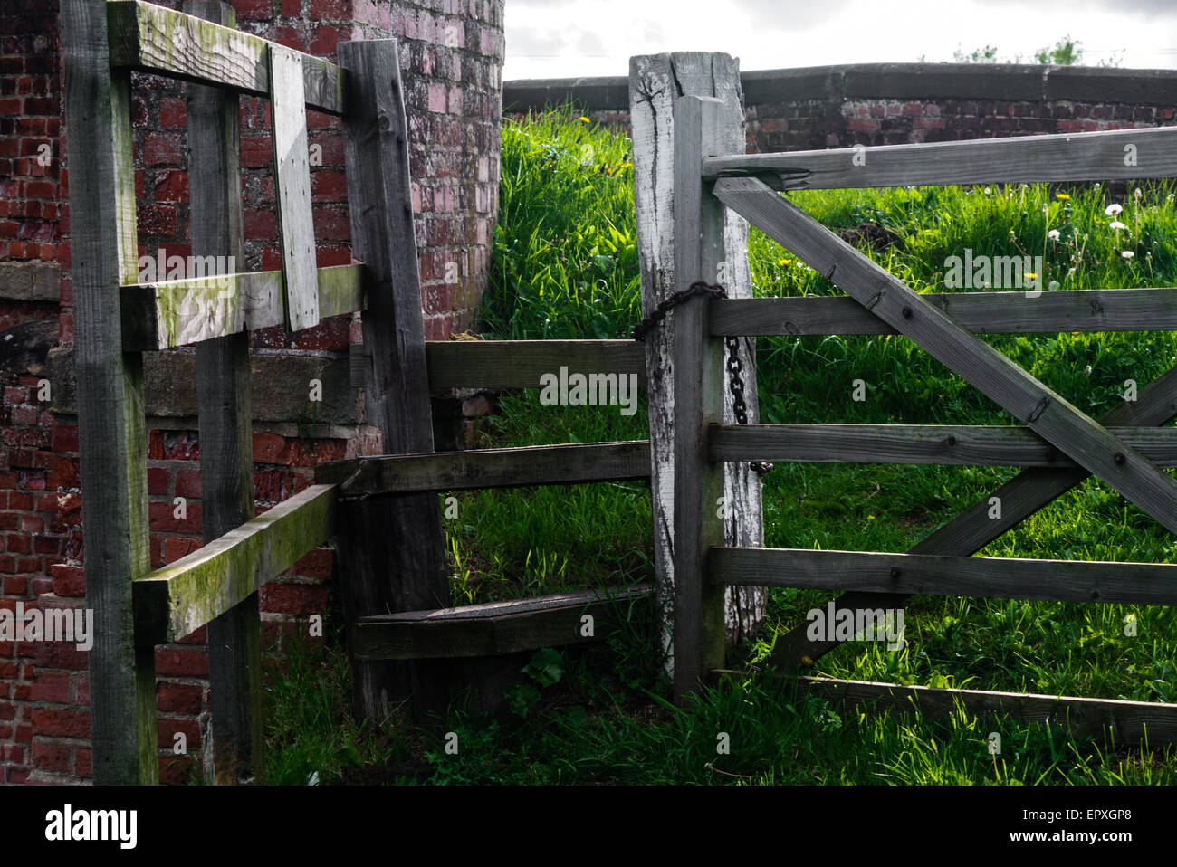 Stile di legno e alla porta accanto a un mattone-costruito un ponte stradale in un ambiente rurale. Foto Stock