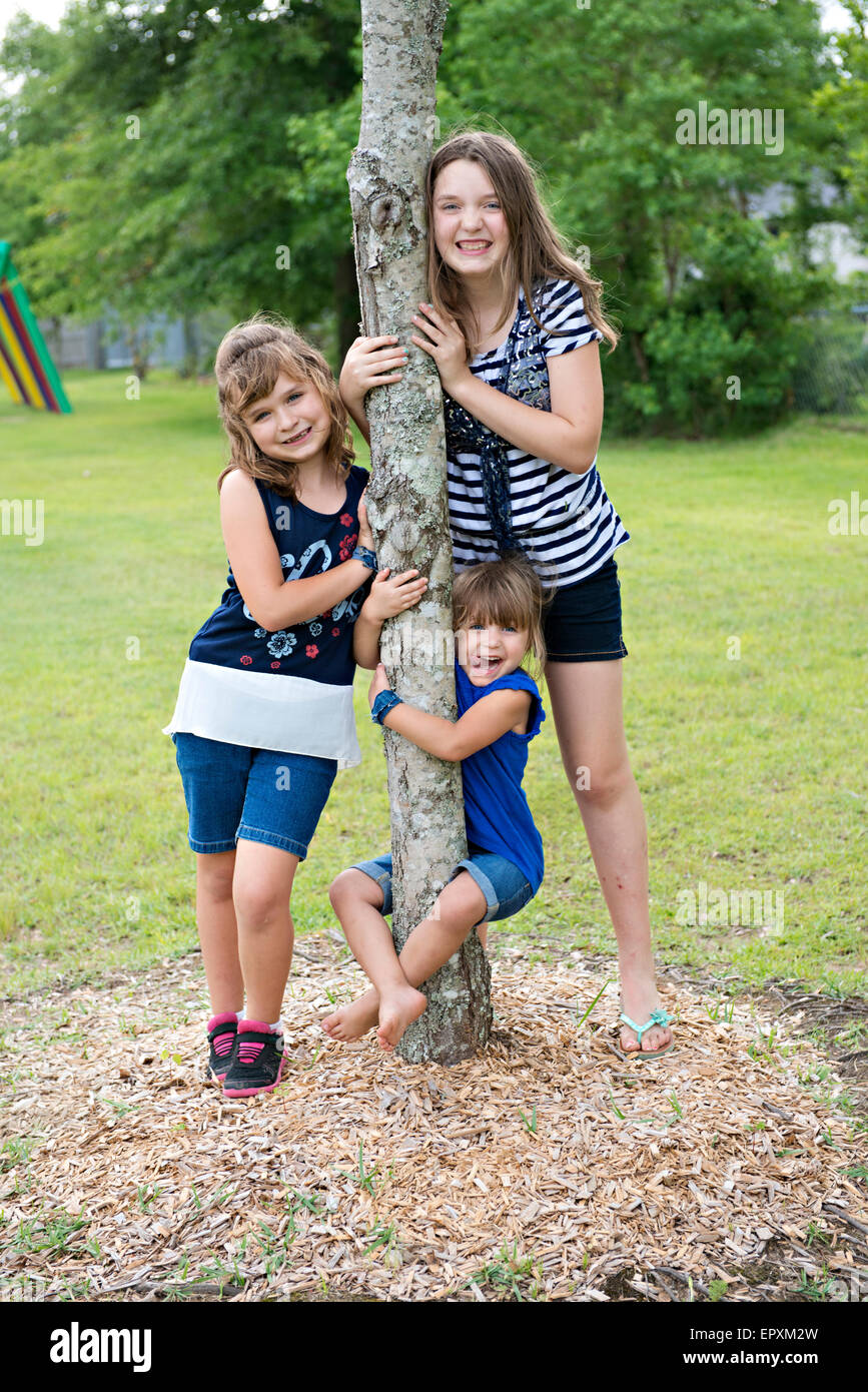 I bambini rappresentano per divertimento ritratto di famiglia in un parco all'aperto il parco giochi mentre è appesa su un tronco di albero Foto Stock