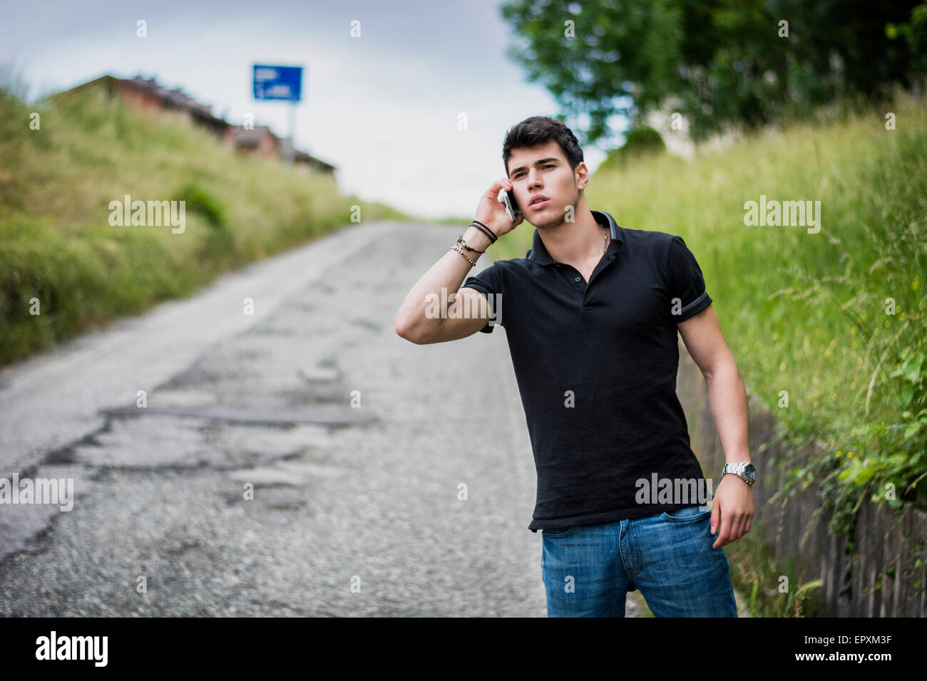 Giovane uomo bello sul lato di una strada, la chiamata sul telefono cellulare e in attesa per il servizio taxi Foto Stock