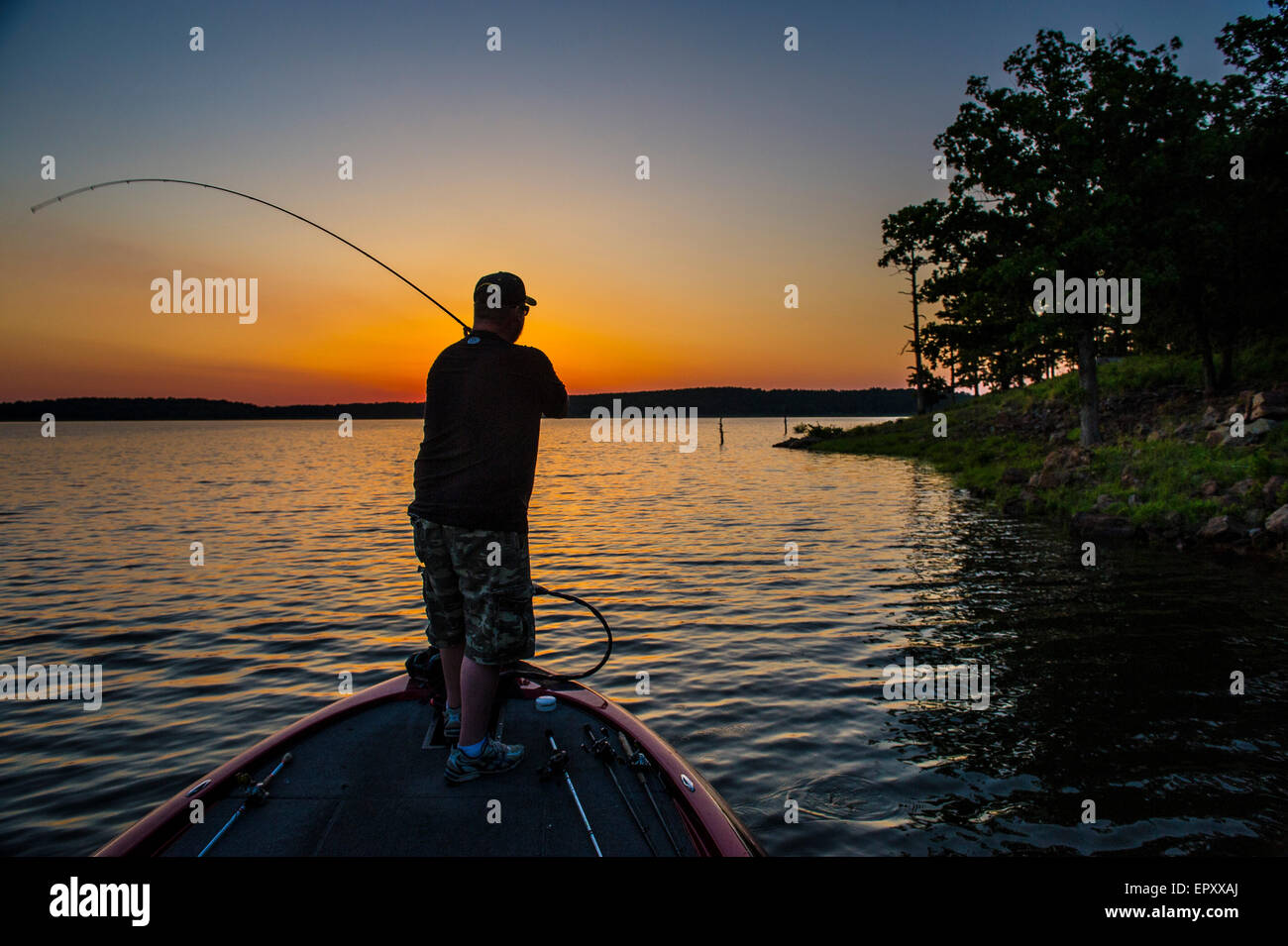Pescatore sulla prua della barca bass FISHING FOR LARGEMOUTH BASS a McGee Creek Lake in Oklahoma al tramonto. Foto Stock