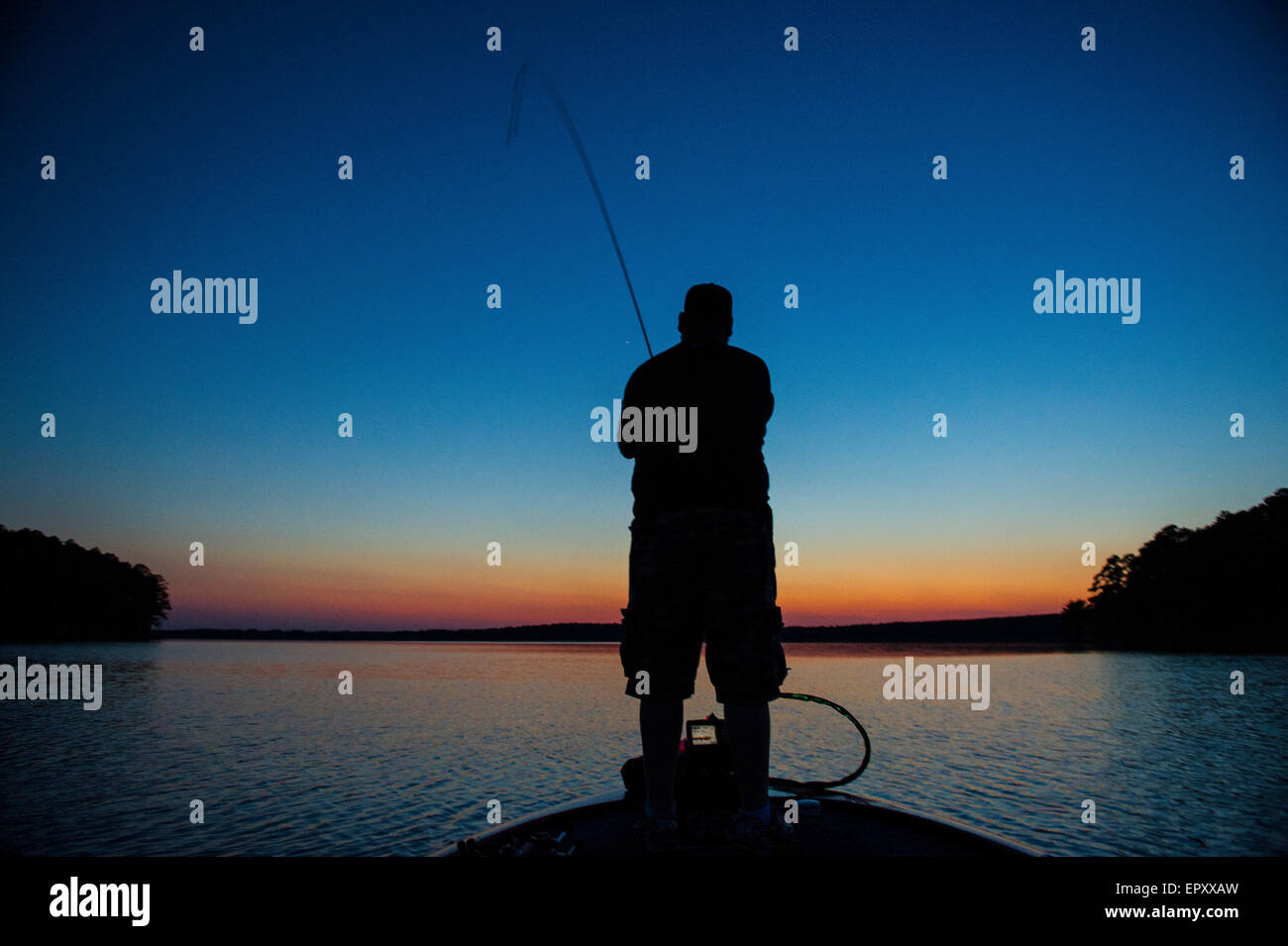 Pescatore sulla prua della barca bass FISHING FOR LARGEMOUTH BASS a McGee Creek Lake in Oklahoma al tramonto. Foto Stock