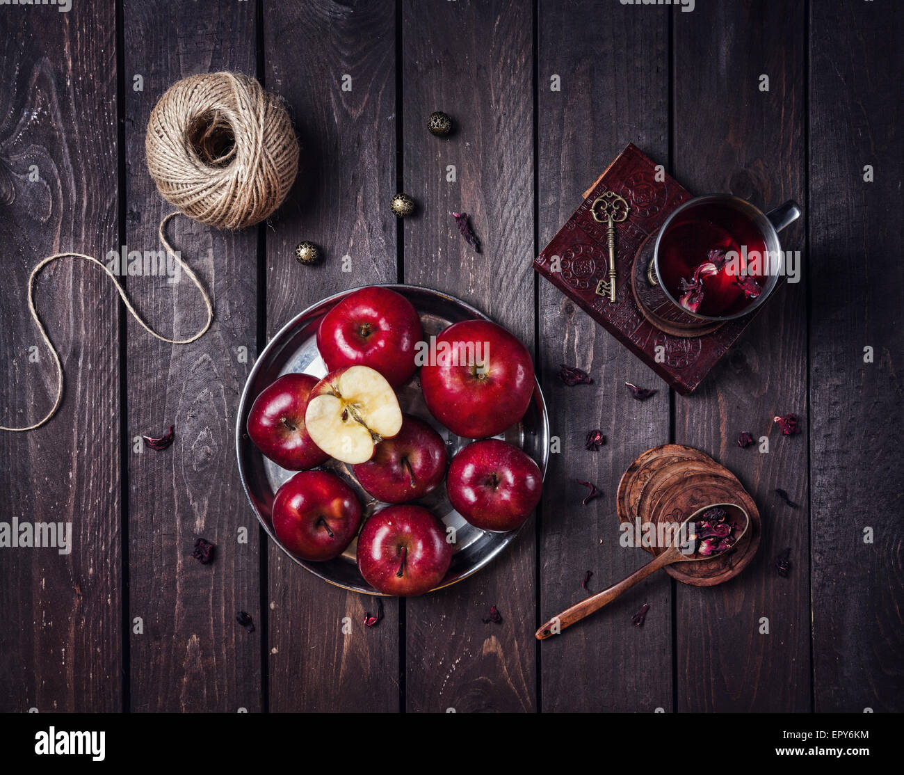 Le mele rosse sulla piastra e la tazza con il tè di ibisco sul vecchio libro al buio sullo sfondo di legno Foto Stock