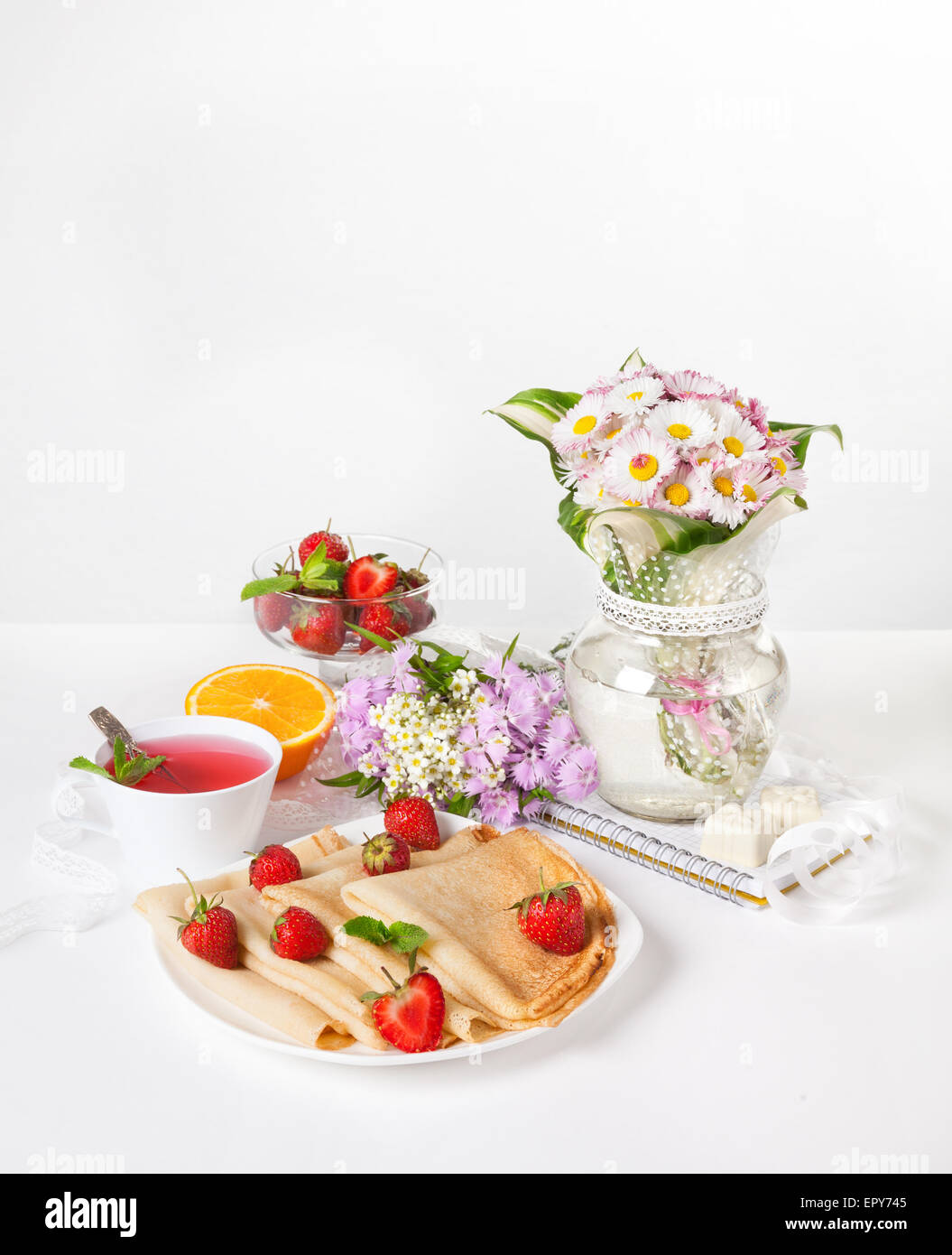 Fragola, frittelle, arancione e hibiscus tè sul tavolo con bouquet di fiori al momento della colazione Foto Stock