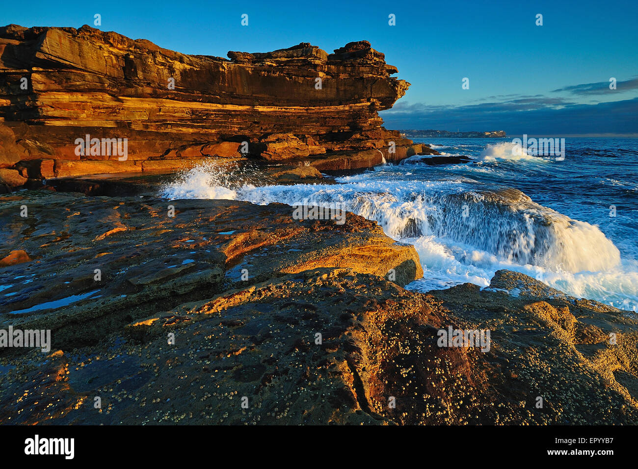 Sunrise seascape con rocce di colore arancione e oceano piscine e conchiglie di mare con nuvoloso cielo tempestoso e scogliere distanti Foto Stock