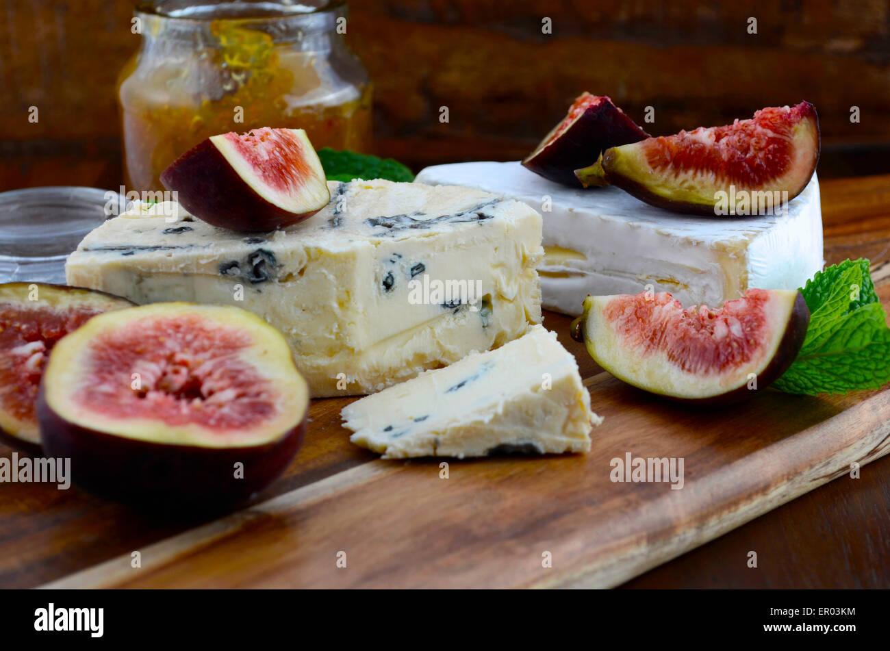 Fichi freschi sul taglio di legno tagliere con vaso di fig jelly preservare e formaggio gourmet sul legno scuro tavolo rustico backgrou Foto Stock
