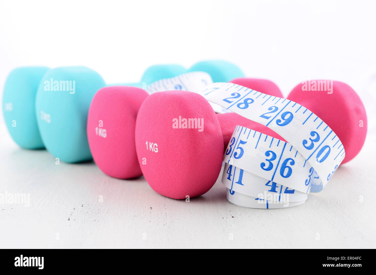 Salute e fitness concetto con colori rosa e blu manubri e nastro di misurazione su bianco invecchiato tavolo di legno dello sfondo. Foto Stock