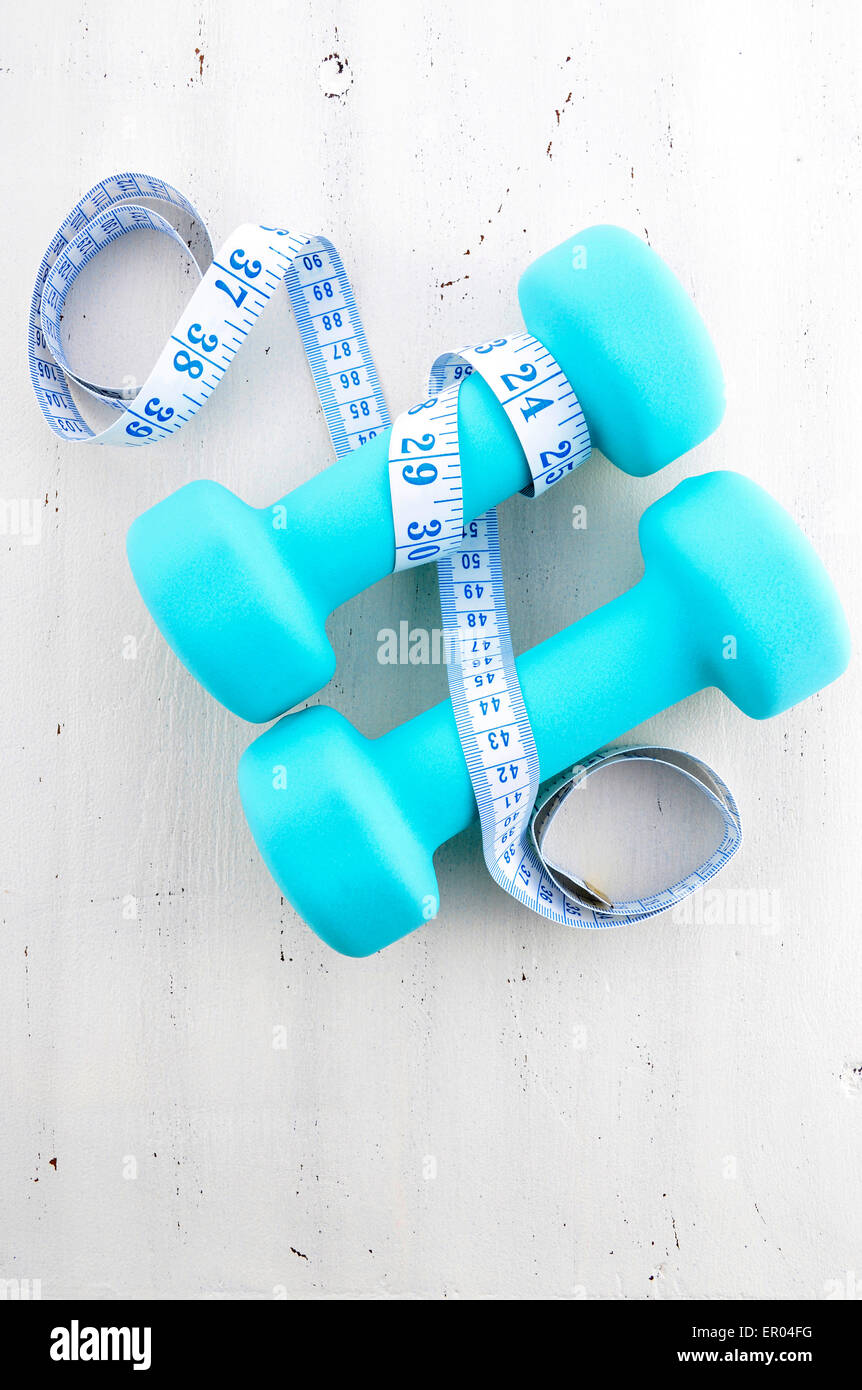 Salute e fitness con il concetto di blu pallido manubri e nastro di misurazione su bianco invecchiato tavolo di legno dello sfondo. Foto Stock