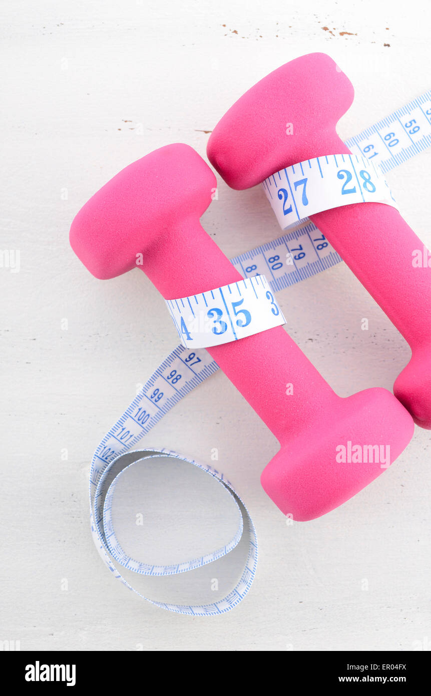 Salute e fitness concetto con manubri rosa e nastro di misurazione su bianco invecchiato tavolo di legno dello sfondo. Foto Stock