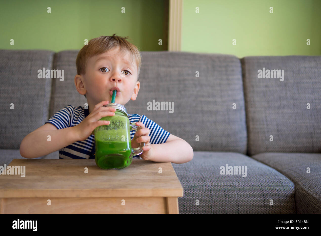 Adorabile bambino bere un frullato verde Foto Stock