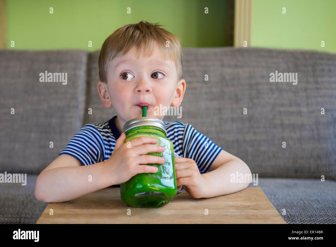 Carino piccolo ragazzo beve un frullato verde Foto Stock