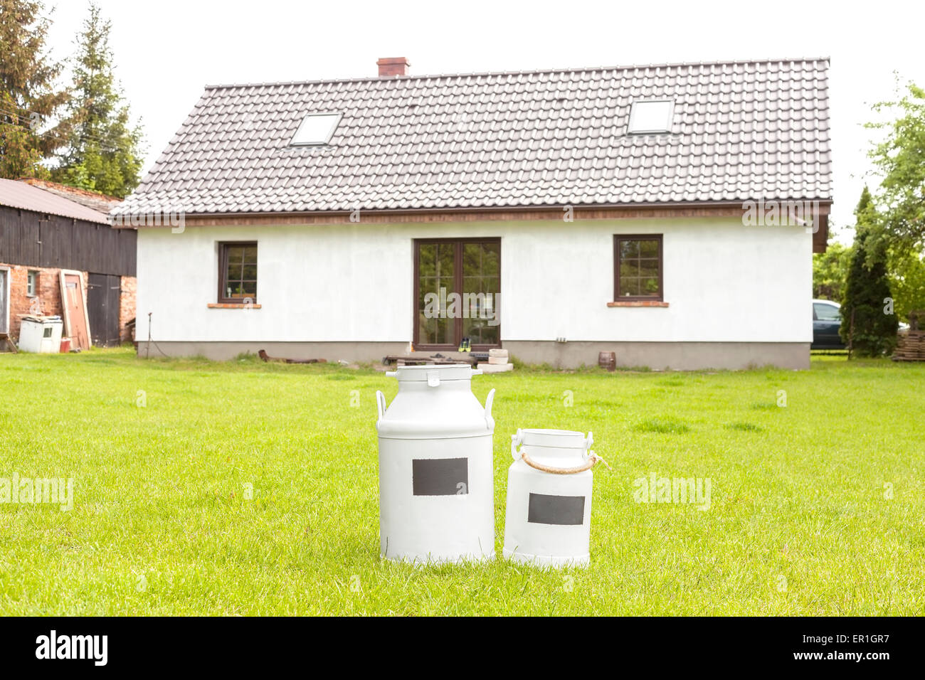 Lattine di latte di fronte a una casa, villaggio rurale dello sfondo. Foto Stock