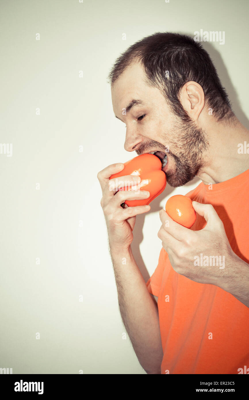 L'uomo (40 anni) azienda mordere orange il peperone mandarine fame Foto Stock