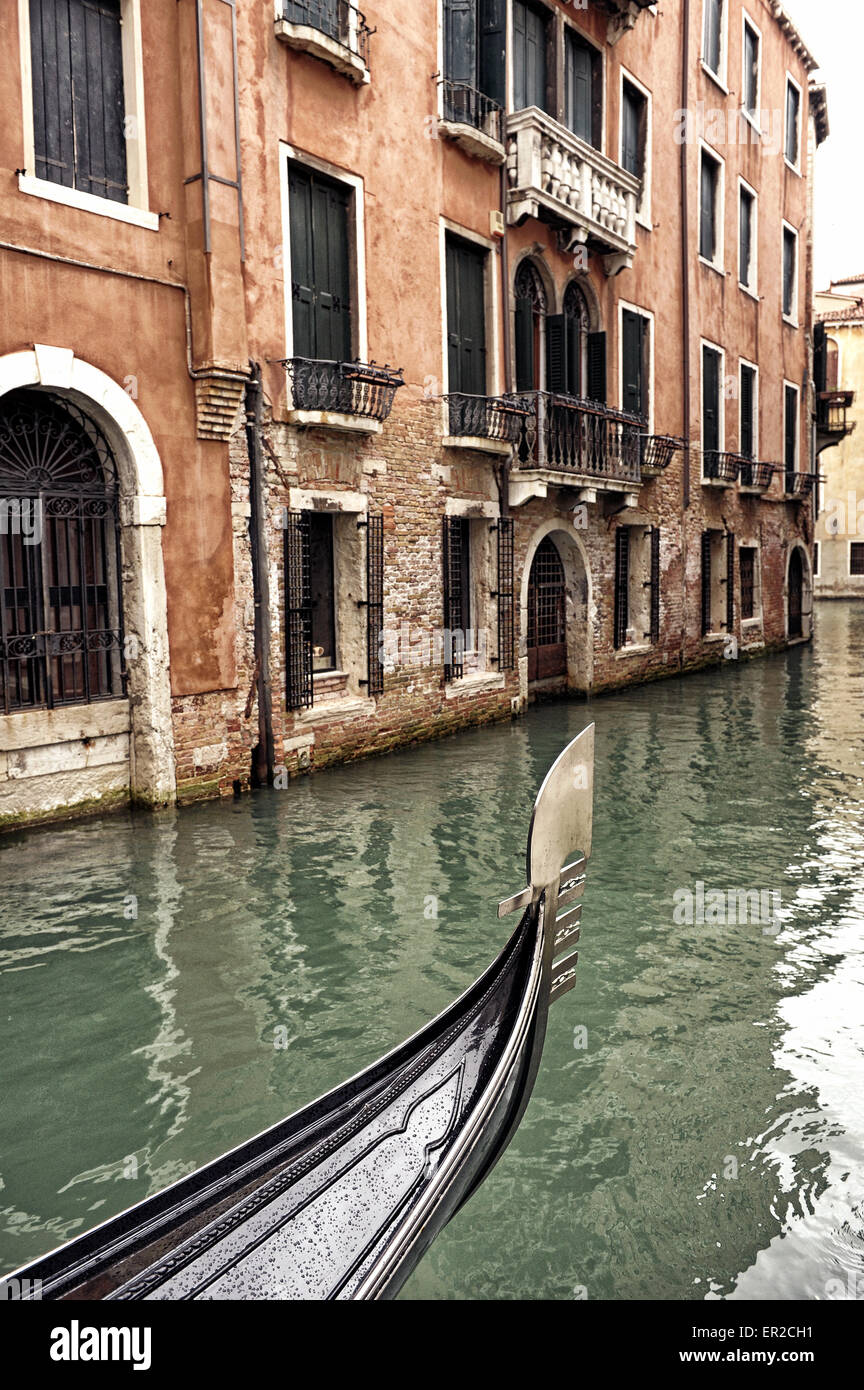 Prua di una gondola veneziana in un giorno di pioggia in un piccolo canale a Venezia, Italia, con gli edifici storici e le antiche porte di acqua Foto Stock