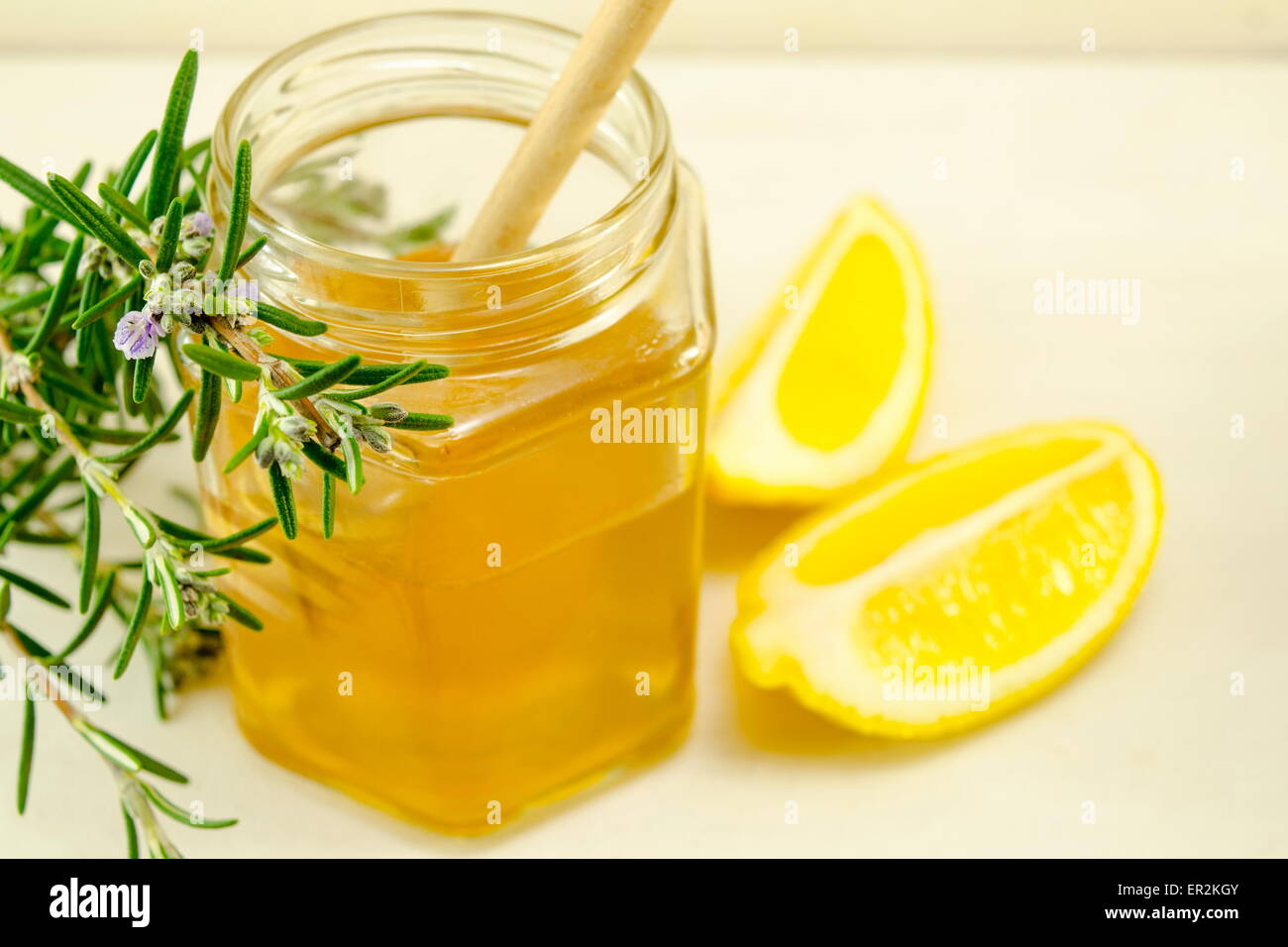 Un vasetto di miele un cucchiaio di legno e limoni su un tavolo Foto Stock