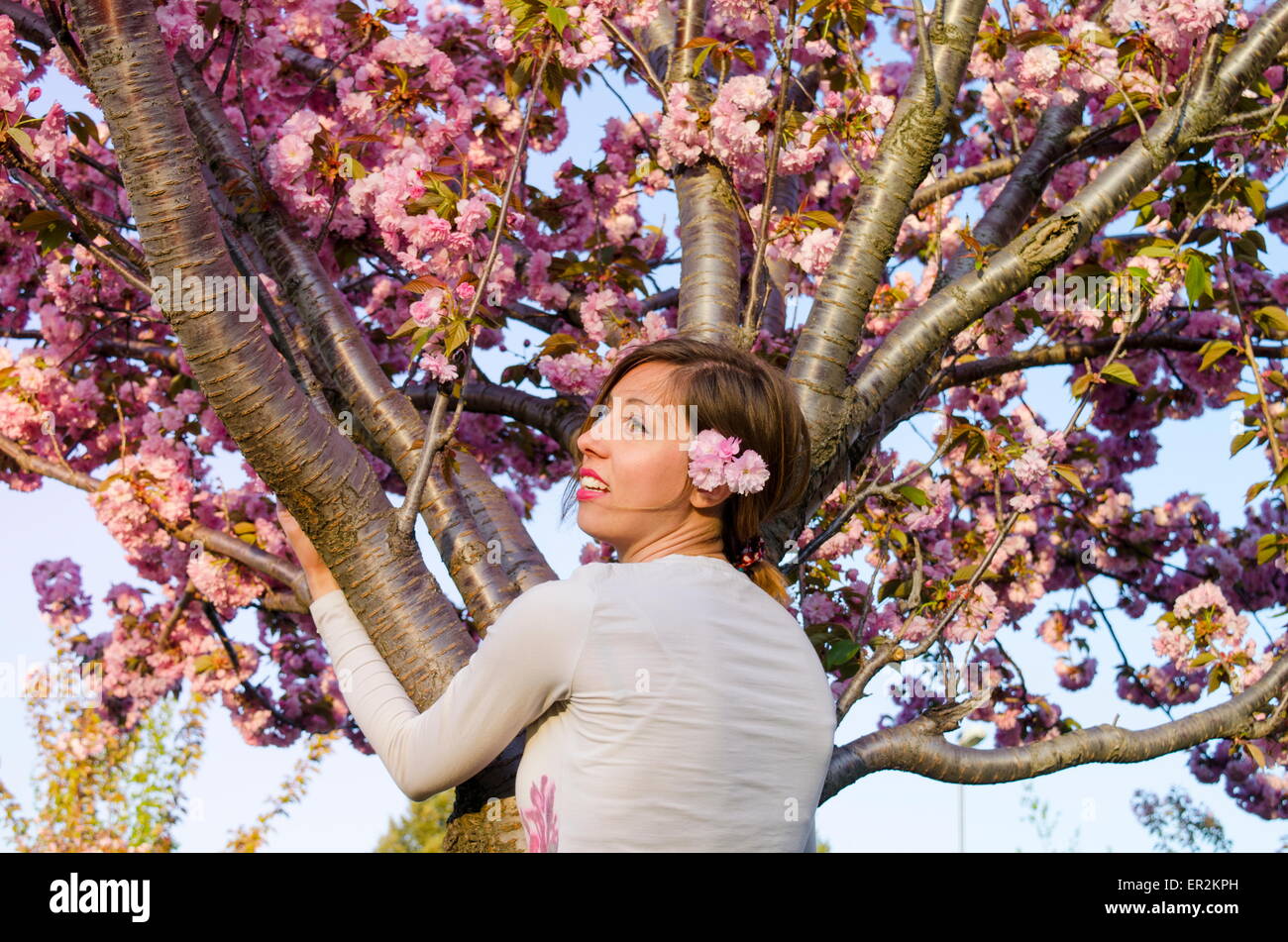 Ragazza giovane con fiori nei capelli abbracciando albero in fiore Foto Stock