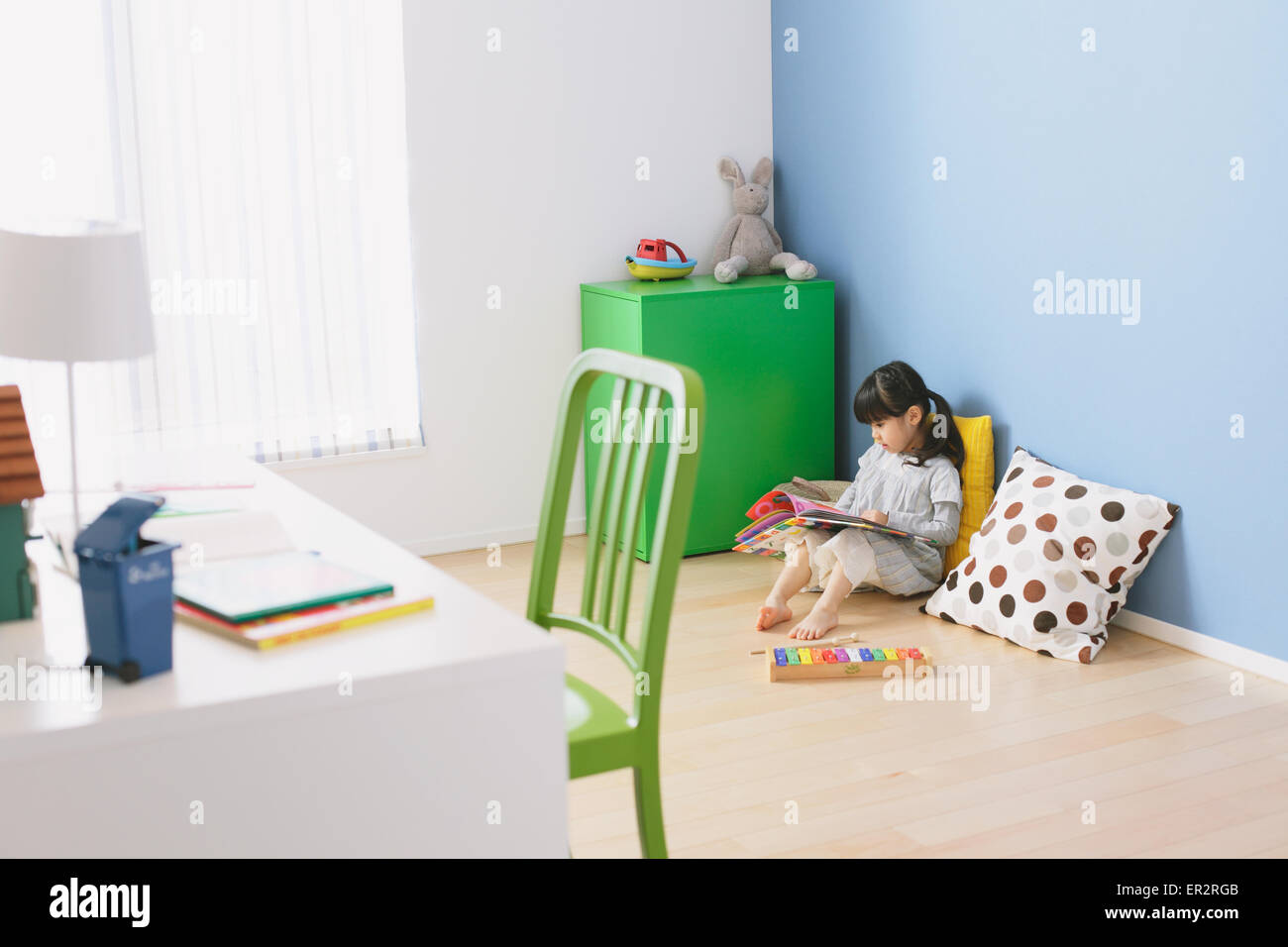 Elementare di età ragazza la lettura di un libro illustrato sul pavimento della stanza dei bambini Foto Stock