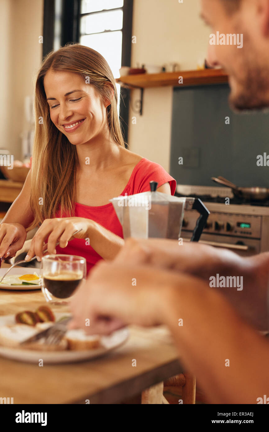 Felice coppia giovane avente la colazione insieme in cucina. Focus sulla donna sorridente mentre mangia e uomo davanti è al di fuori della messa a fuoco si Foto Stock